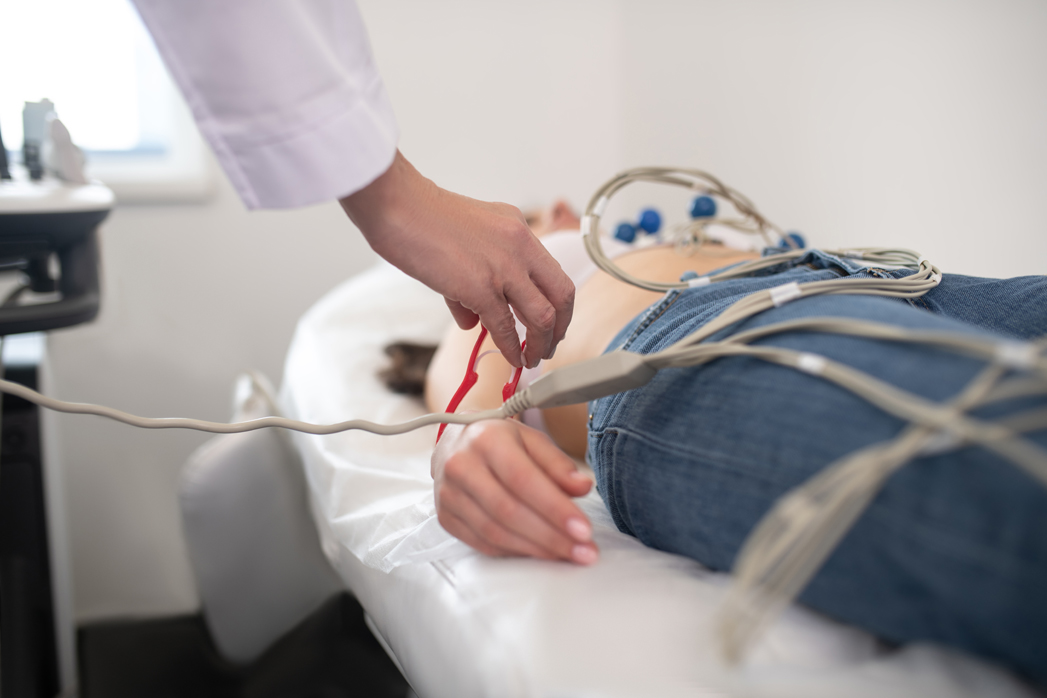 Procedure. Doctor in white robe making electrocardiogram to the patient laying on the couch
